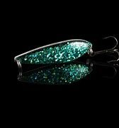 Glittrande fiskeagn i grönt och silver med krok, reflekterande bakgrund.